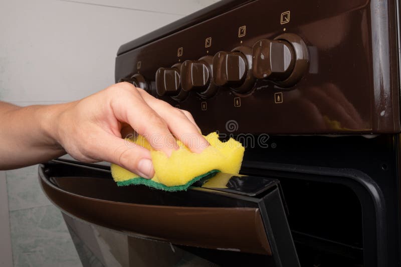 Cleaning the surface on a gas oven with a yellow washcloth, cleaning the kitchen.
