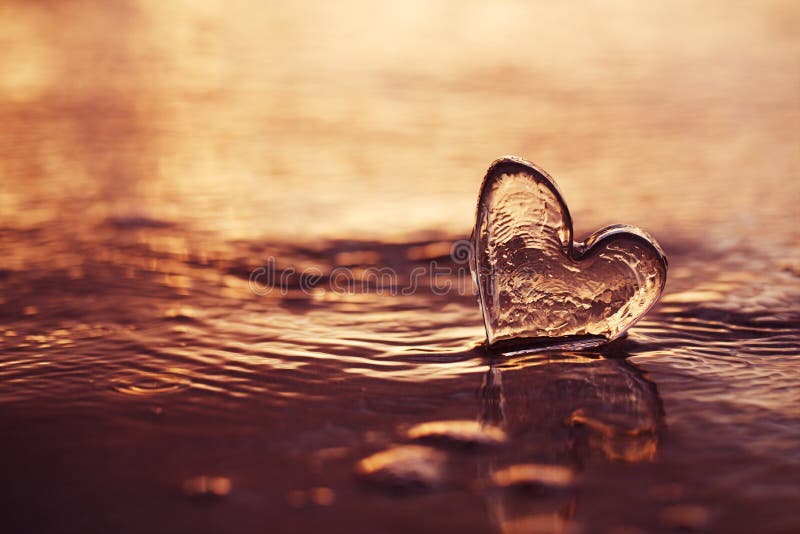 Clear glass heart on  sand beach with sunrise sun light