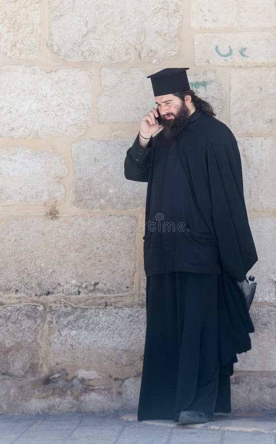 The clergyman stands and talks on his mobile phone in the old city of Jerusalem, Israel.