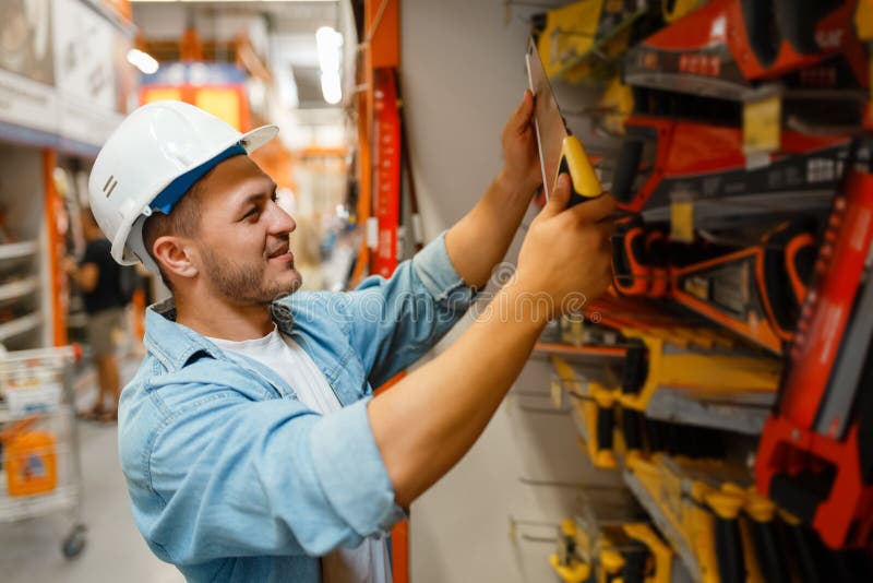 Homme Constructeur Choisissant La Ceinture à Outils Sur L'étagère En  Quincaillerie. Constructeur En Uniforme Regarde Les Marchandises Dans La  Boutique De Bricolage