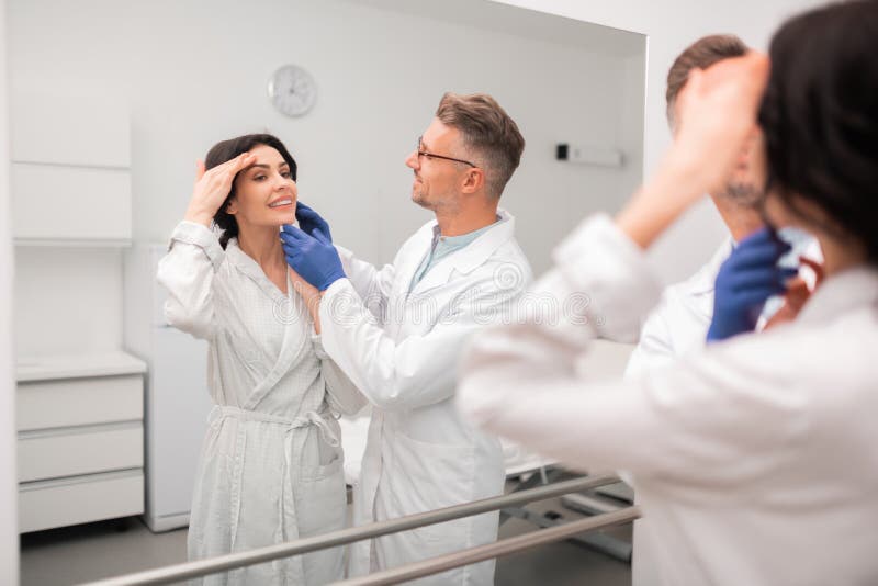 Plastic Surgeon and Client Looking into Mirror after Surgery Stock