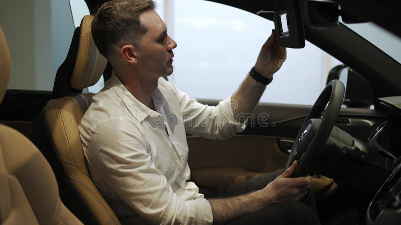 Cliente con camisa blanca sentado en salón de coches espejo táctil quiere comprar nuevo automóvil en la sala de exposición almacen de metraje de vídeo