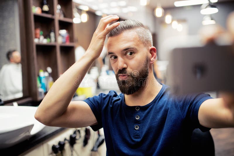 Cliente do homem do moderno na barbearia, fazendo as caras engraçadas ao tomar o seflie fotografia de stock Cliente do homem do moderno na barbearia, fazendo as caras engraçadas ao tomar o seflie fotografia de stock
