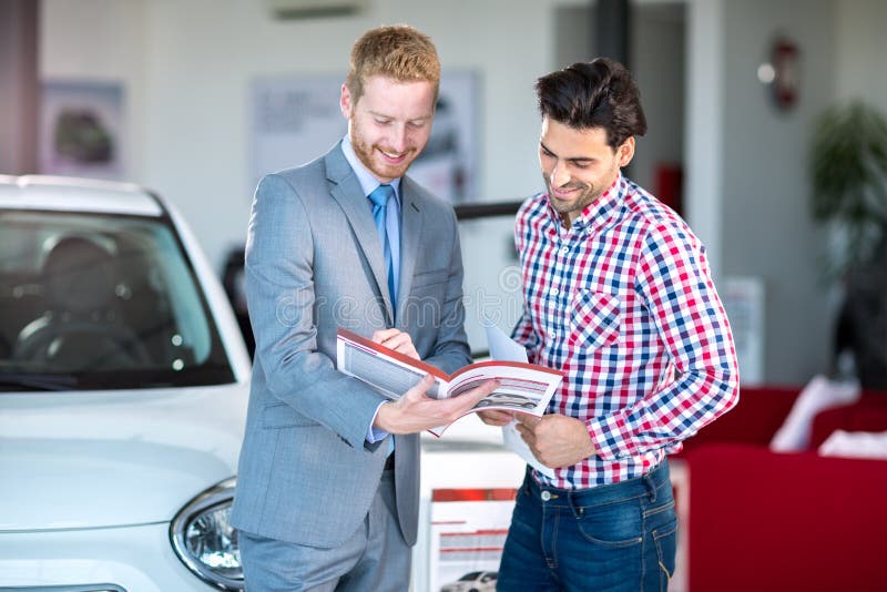 Cliente maschio del maschio e del rappresentante al salone del concessionario auto fotografia stock libera da diritti Cliente maschio del maschio e del rappresentante al salone del concessionario auto fotografia stock libera da diritti