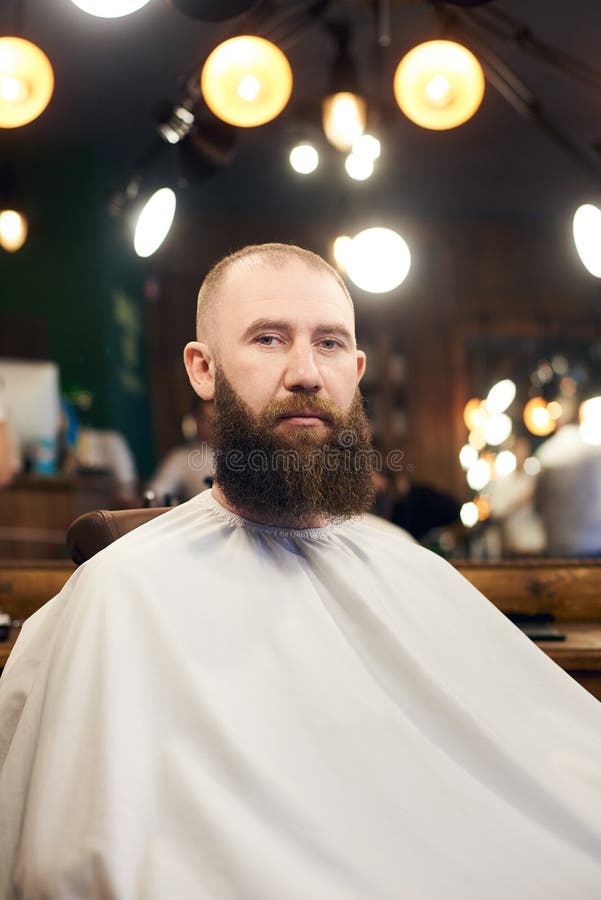 Cliente masculino com a barba que senta-se na cadeira do cabeleireiro Homem s?rio com a barba marrom longa Estilo popular moderno fotos de stock royalty free Cliente masculino com a barba que senta-se na cadeira do cabeleireiro Homem s?rio com a barba marrom longa Estilo popular moderno fotos de stock royalty free