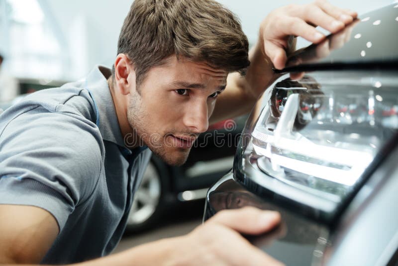 Cliente masculino que examina e que olha com cuidado em um carro novo imagem de stock Cliente masculino que examina e que olha com cuidado em um carro novo imagem de stock