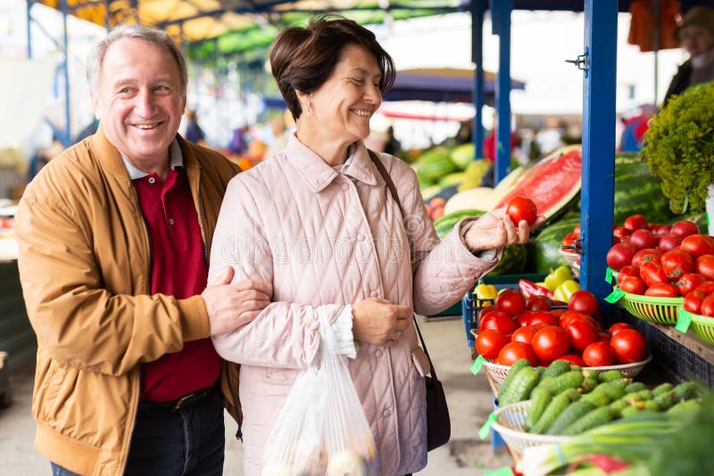 Clientes ocasionales de hombres y mujeres mayores que compran tomates frescos en el mercado interior foto de archivo libre de regalías