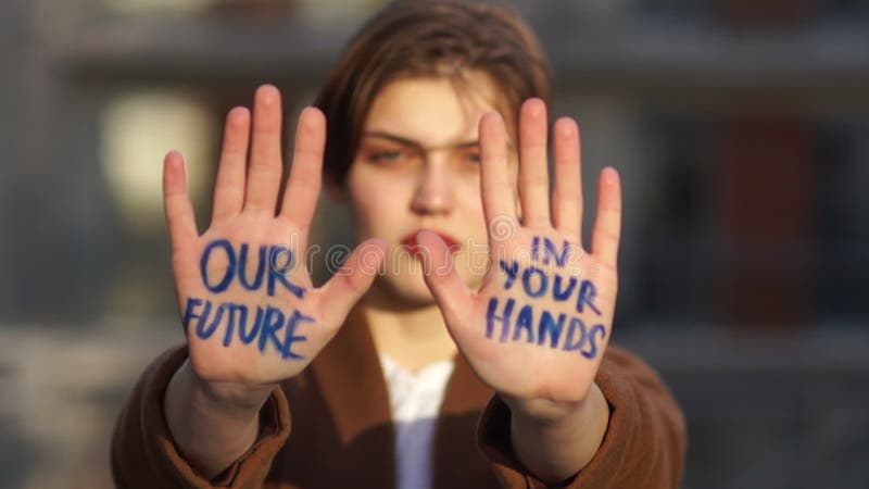 Climat strike, environmental disaster. Close portrait of a beautiful student with an inscription on the palms. Our