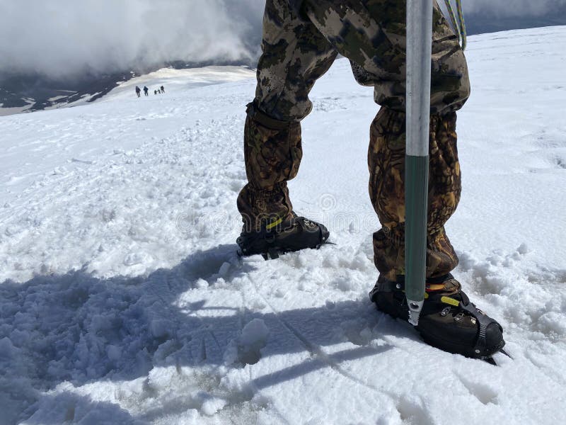 Climber`s legs in cats and ice ax close-up on a snowy slope of the northern Elbrus region