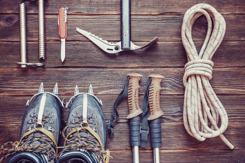 Climbing equipment: rope, trekking shoes, crampons, ice tools, ice ax, ice screws, red knife and other set on dark wooden