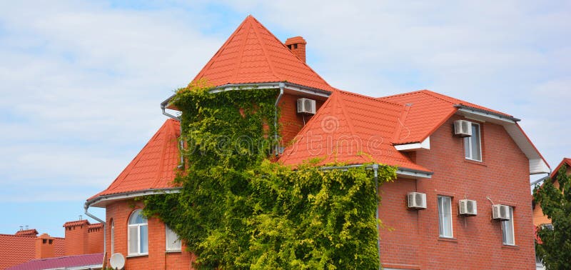 Climbing ivy coveres the facade of a brick house for passive cooling and thermal comfort. Brick house with air conditioning (AC) units on the facade outdoors.