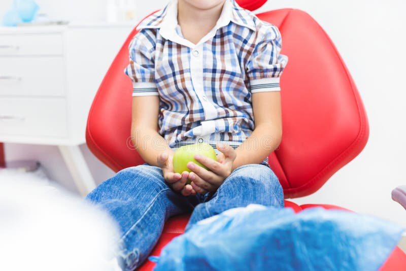 Clinique dentaire Réception, examen du patient Soin de dents Peu garçon tenant une pomme tout en se reposant dans un dentaire image stock Clinique dentaire Réception, examen du patient Soin de dents Peu garçon tenant une pomme tout en se reposant dans un dentaire image stock
