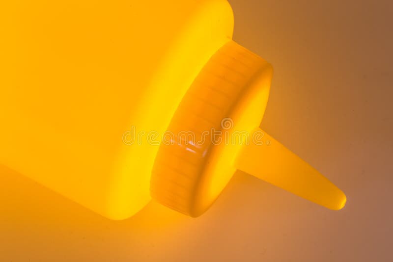 Clloseup en plastique jaune de bouteille de moutarde avec une lumière rougeoyante photographie stock libre de droits Clloseup en plastique jaune de bouteille de moutarde avec une lumière rougeoyante photographie stock libre de droits