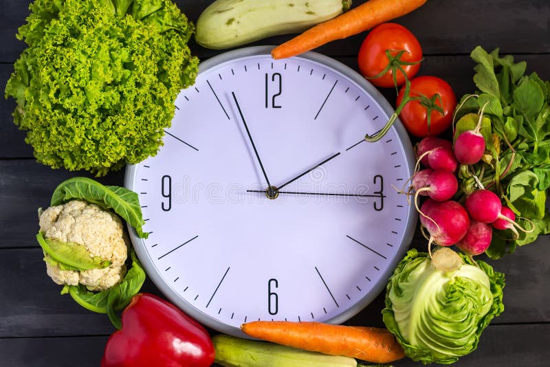 Clock and fresh vegetables. Zucchini, bell peppers, carrots, cabbage, cauliflower, radish, lettuce, tomato. Concept of a healthy d