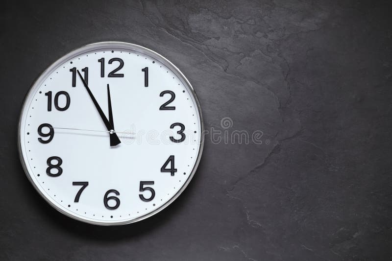 Clock Showing Five Minutes until Midnight on Black Table, Top View with Space for Text. New Year