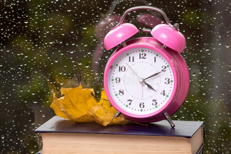Clock and yellow maple leaf on a book against a window with drops of rain on the glass_ stock images Clock and yellow maple leaf on a book against a window with drops of rain on the glass_ stock images