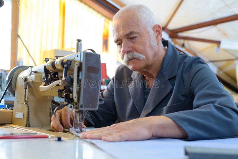 Close-aged man repairs fabric with old sewing machine stock photo