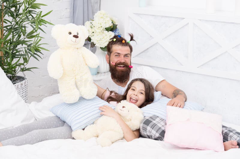 Close friends. Dad and girl relaxing in bedroom. Pajamas style. Father bearded man with funny hairstyle ponytails and royalty free stock photography Close friends. Dad and girl relaxing in bedroom. Pajamas style. Father bearded man with funny hairstyle ponytails and royalty free stock photography