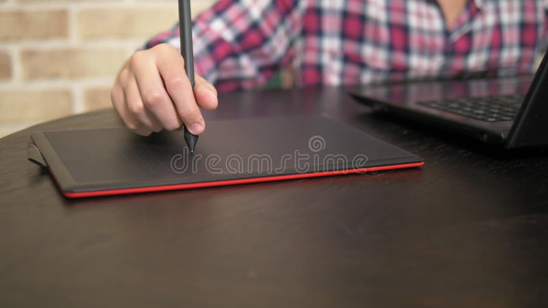 Close. Hand of a teenager boy in a plaid shirt using a stylus. works on a graphic tablet stock video