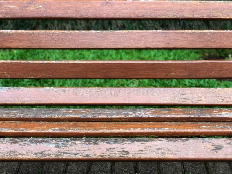 A close image of a wooden bench with grass background and concrte blocks floor royalty free stock image