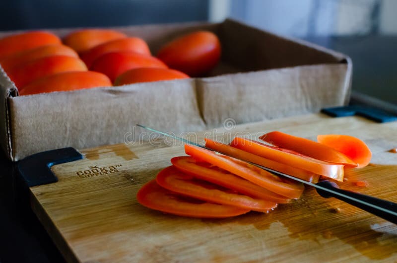 Close shot of a sliced tomatoe. Box with tomatoes on the bakground