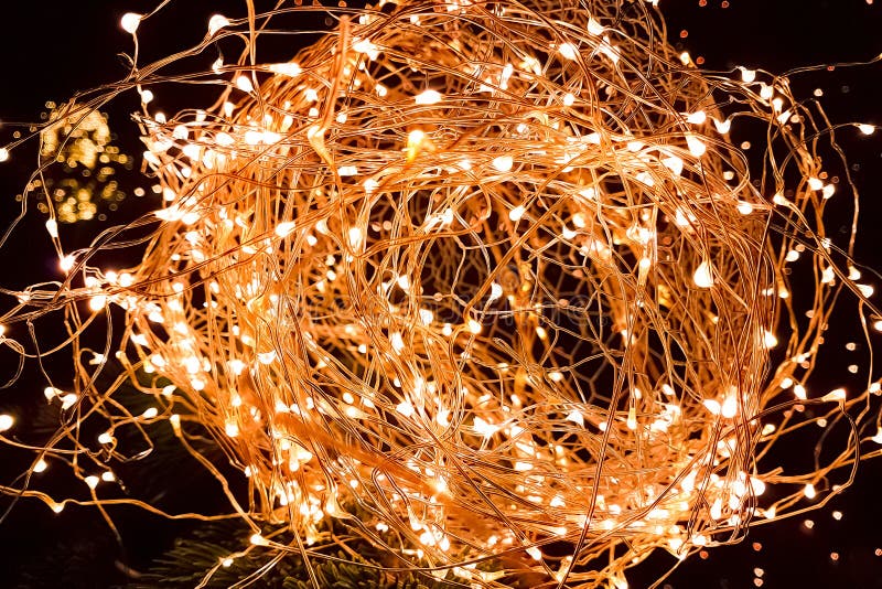 Close-up of abstract Christmas glitter lights ball on xmas tree with warm sparkle bokeh on black background, concept of golden holiday xmas decoration