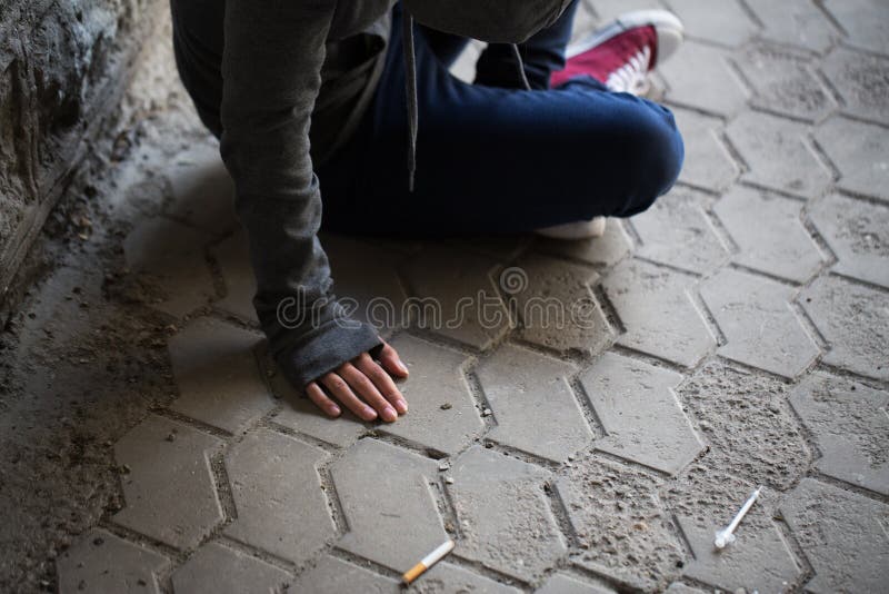 Substance abuse, addiction, people and drug use concept - close up of addict woman and used syringes on ground. Substance abuse, addiction, people and drug use concept - close up of addict woman and used syringes on ground