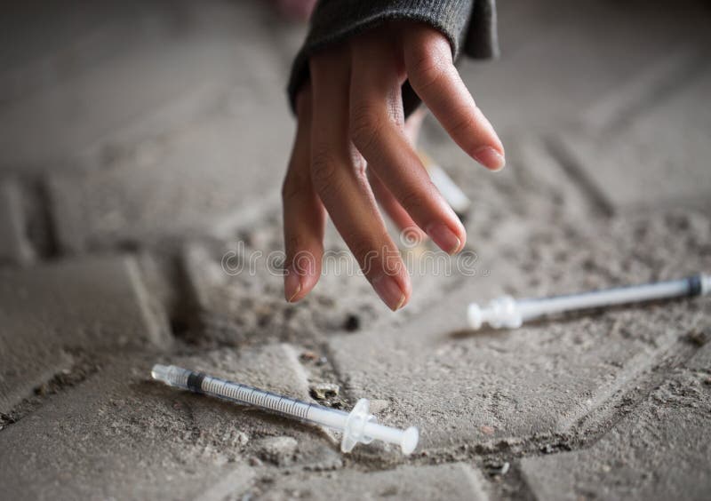 Substance abuse, addiction, people and drug use concept - close up of addict woman hands and used syringes on ground. Substance abuse, addiction, people and drug use concept - close up of addict woman hands and used syringes on ground