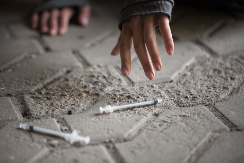 Substance abuse, addiction, people and drug use concept - close up of addict woman hands and used syringes on ground. Substance abuse, addiction, people and drug use concept - close up of addict woman hands and used syringes on ground