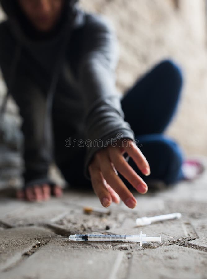 Substance abuse, addiction, people and drug use concept - close up of addict woman reaching to used syringes on ground. Substance abuse, addiction, people and drug use concept - close up of addict woman reaching to used syringes on ground