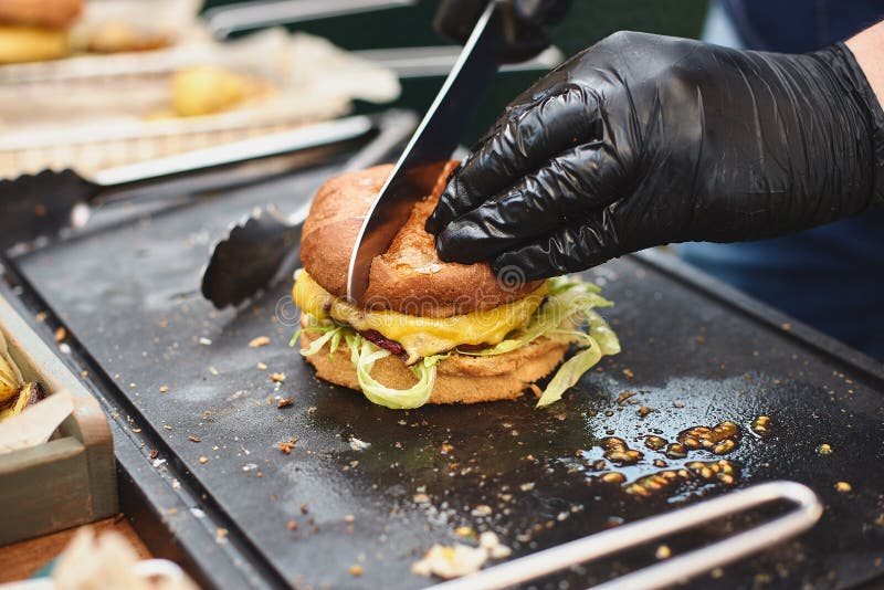Close up of appetising beef burger. Chef`s hands divide into half cooked hamburgers from beef. Street food ready to stock photos Close up of appetising beef burger. Chef`s hands divide into half cooked hamburgers from beef. Street food ready to stock photos