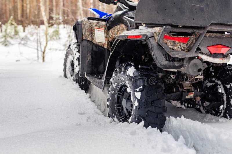 Close-up ATV 4wd quad bike in forest at winter. 4wd all-terreain vehicle stand in heavy snow with deep wheel track. Seasonal