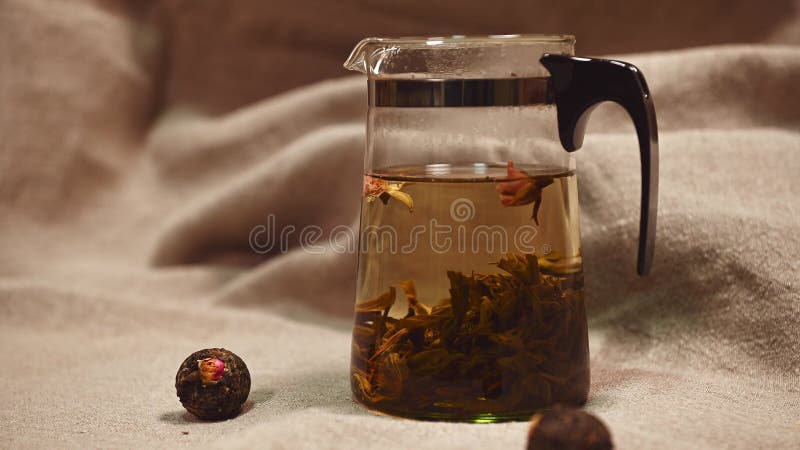 Close-up: A ball of green bound Chinese fragrant tea with an opening flower in a transparent teapot with boiling water stock footage