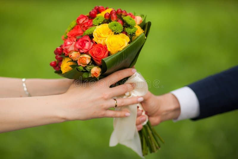 Close up of beautiful bouquet of fresh flowers. man and woman hands. happy bride, groom over summer green park background.
