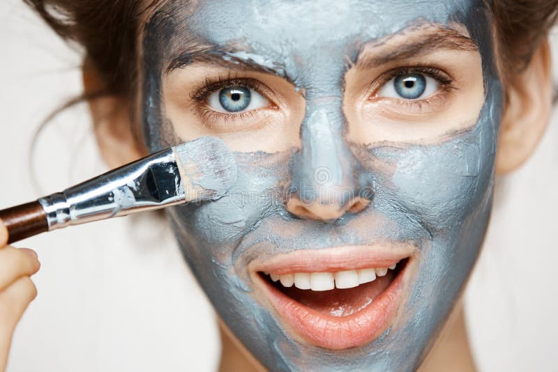 Close up of beautiful girl in hair curlers smiling looking at camera covering face with mack. Facial treatment. Beauty