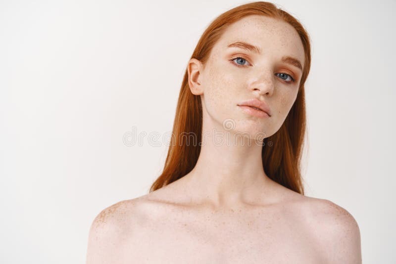 Close-up of beautiful woman with ginger hair and blue eyes, pale skin, looking at camera confident, standing naked on