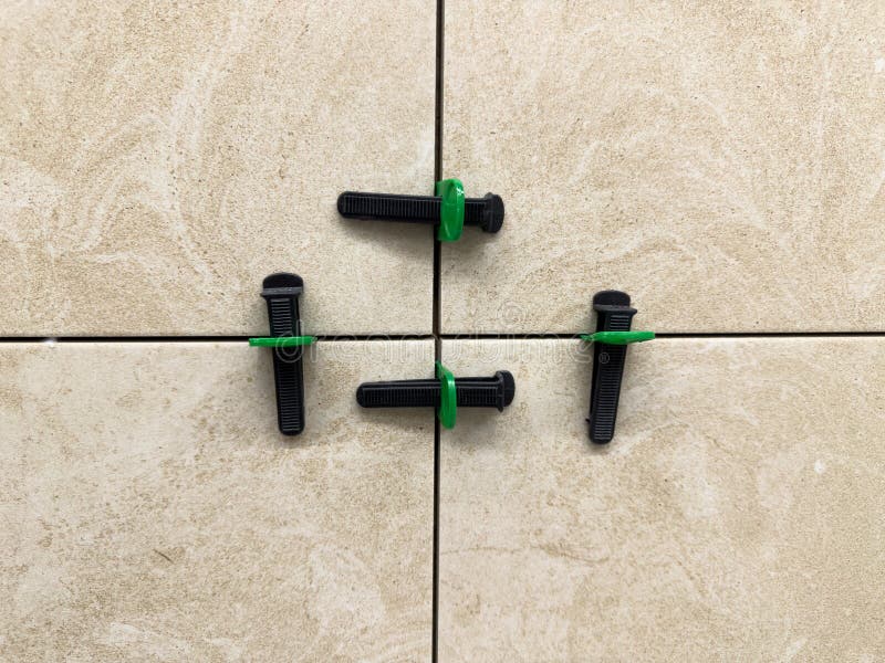 Close up of beige ceramic tiles aligned with tile leveling system. Precision tools create straight grout lines and a smooth stock image