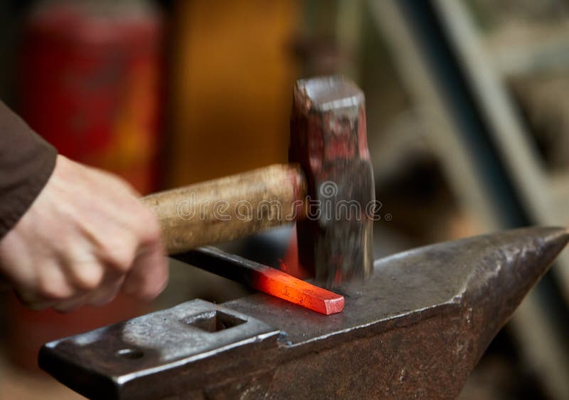 Close-up of a blacksmith`s hands manipulating a metal piece above his forge, selective focus.