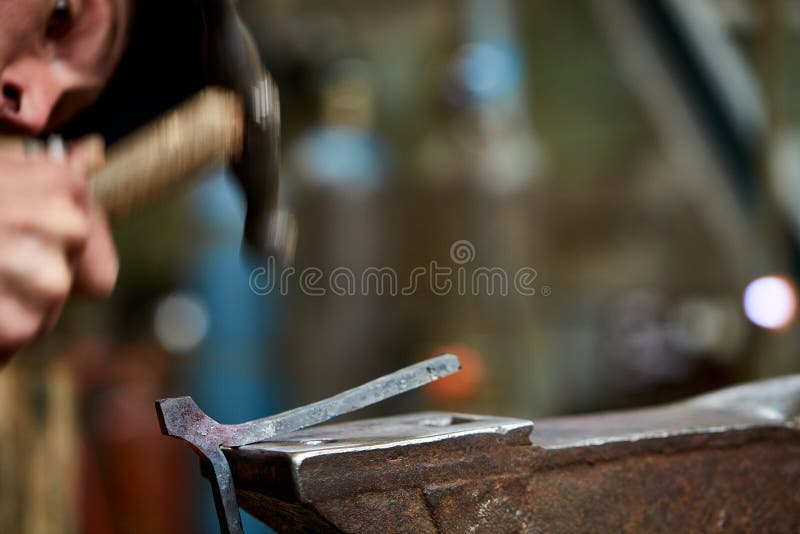 Close-up of a blacksmith`s hands manipulating a metal piece above his forge, selective focus.