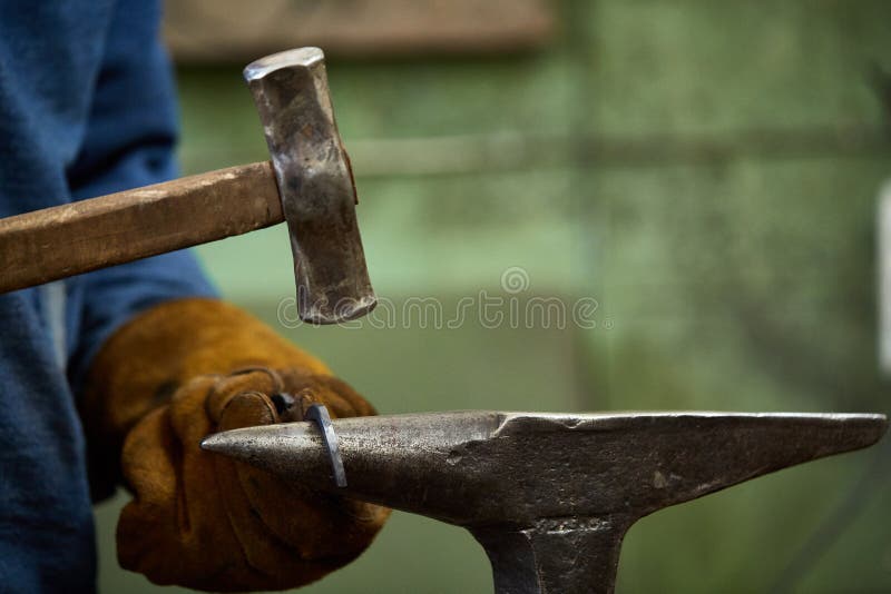 Close-up of a blacksmith`s hands manipulating a metal piece above his forge, selective focus. Manual, burning.