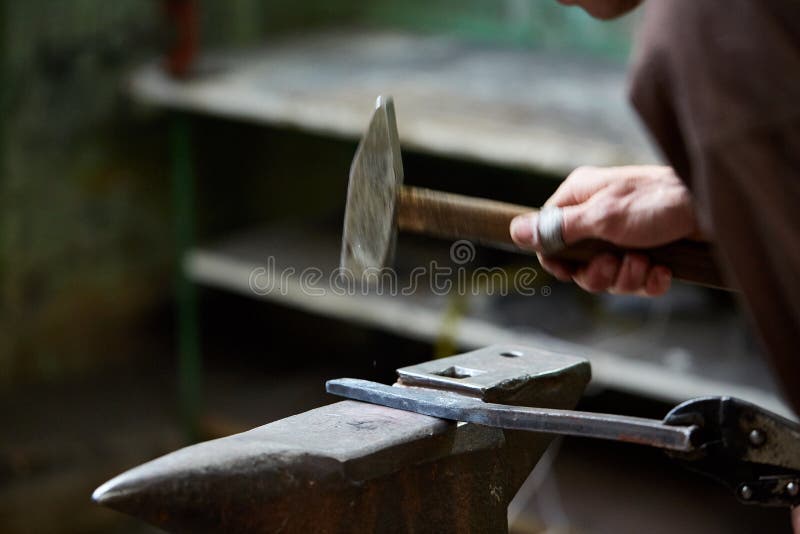 Close-up of a blacksmith`s hands manipulating a metal piece above his forge, selective focus.
