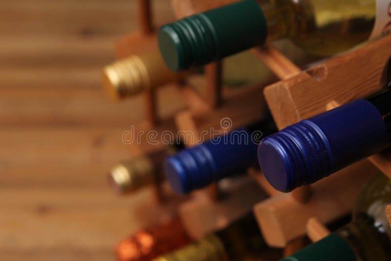 Close up of blue top wine bottle with other bottles in a wooden wine rack.