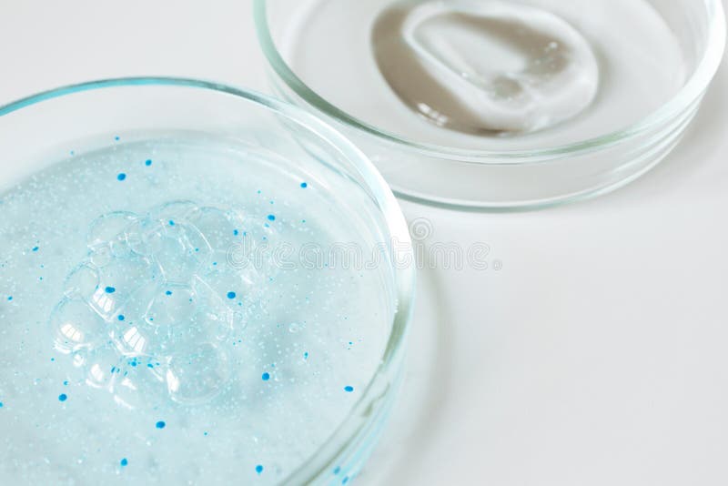 Close-up blue shower gel with scrub grain with bubbles and transparent shampoo smudge in glass petri dish with selective focus