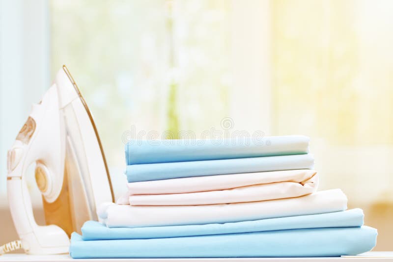 Close-up of blue and white clean bedding on a blurred background. A stack of folded bedsheets on the table, an iron stands nearby. royalty free stock photos