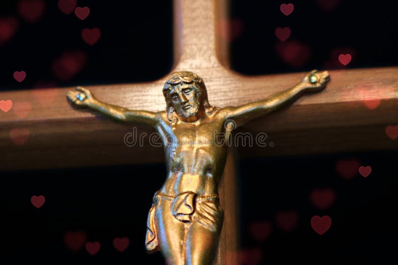 Close up of crucifix with gold Christ on wood cross durrounded by red hearts