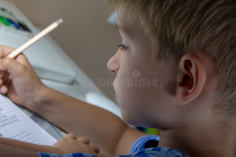 Close-up of boy hand with pencil writing English words. The boy writes his first test on English. Child writing. Elementary, board.