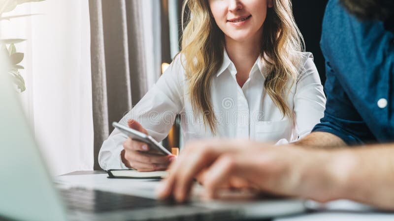 Close-up. Businessman and businesswoman sitting at table in front of laptop and looking at monitor. Man is typing on laptop. Woman holds smartphone in her hand and looks at monitor. Online marketing.