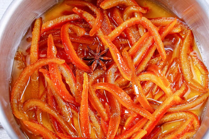 Close-up of Homemade candied orange and lemon peels cooked in boiling syrup with cinnamon, nutmeg and anise star in pot, view from above. Close-up of Homemade candied orange and lemon peels cooked in boiling syrup with cinnamon, nutmeg and anise star in pot, view from above