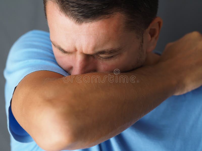 Caucasian male coughs in his elbow.