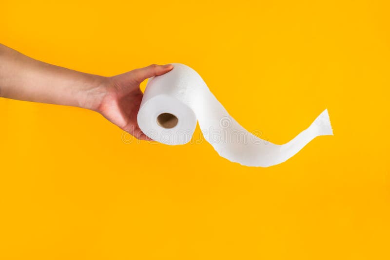 Close up caucasian male hand holding or giving a roll of toilet paper with flying tissue on bright yellow background. Crisis